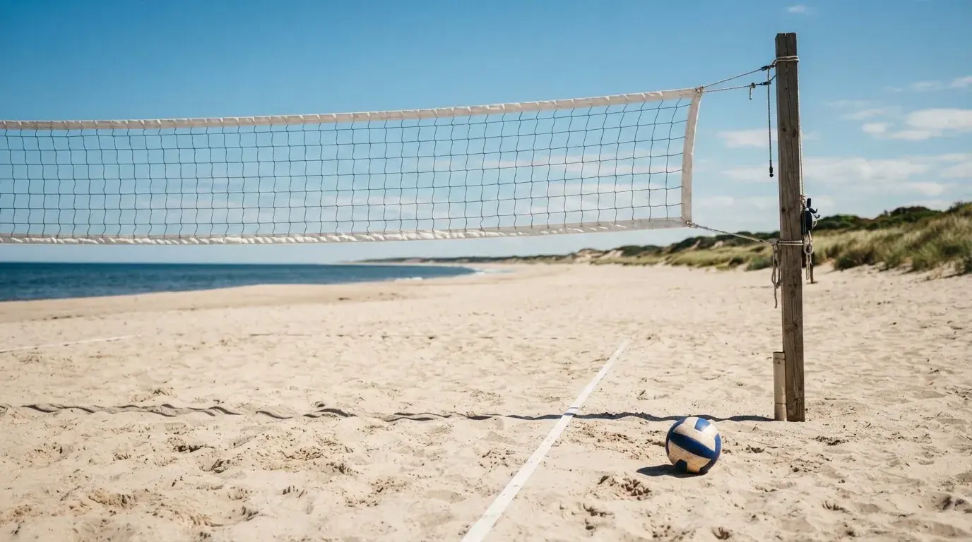 Siatka do siatkówki rozpięta nad piaszczystym boiskiem plażowym pod czystym niebem.