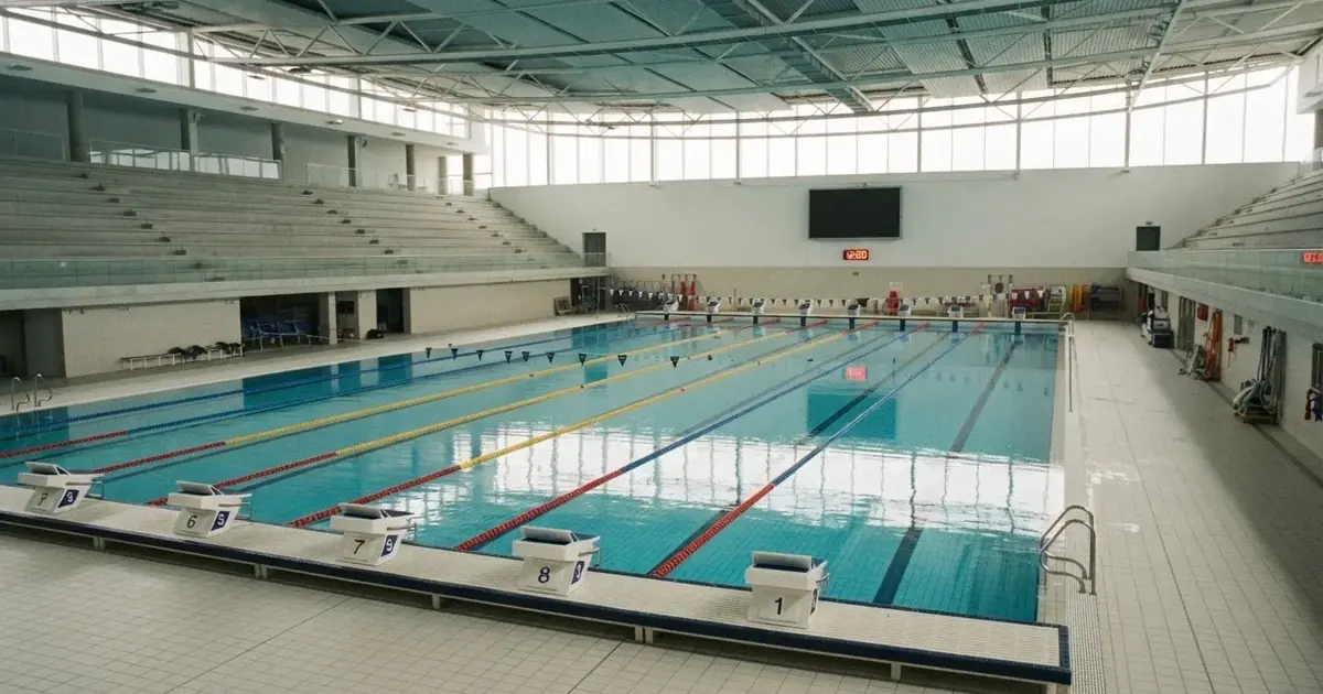 Pusty basen olimpijski z równymi torami i spokojną taflą wody, widok z trybun w jasnym świetle.